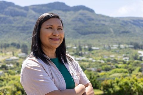 Asian woman smiling with arms crossed overlooking green valley and mountain views