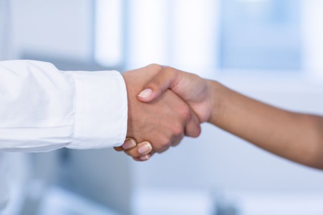 Close-up of a doctor and patient shaking hands in a hospital setting. This image can be used to represent trust, agreement, and partnership in healthcare. Ideal for medical websites, healthcare brochures, and patient care articles.