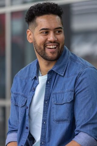 Young man smiling casually in denim shirt leaning outdoors near modern glass building