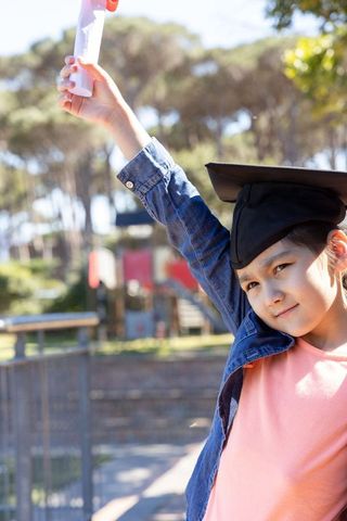 Young asian girl celebrating graduation holding diploma outdoors wearing mortarboard