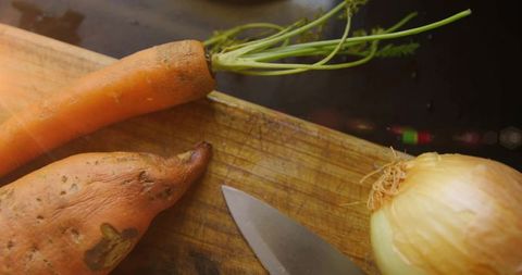 Preparing rustic vegetables: dirt-speckled carrot, sweet potato and onion on wooden cutting board