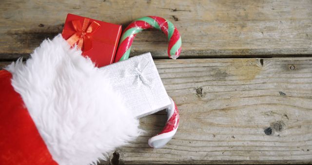 A Santa hat, a candy cane, and a gift box are placed on a rustic wooden surface, symbolizing holiday celebrations and gift-giving traditions. These items evoke the festive spirit of Christmas and the joy of sharing presents.