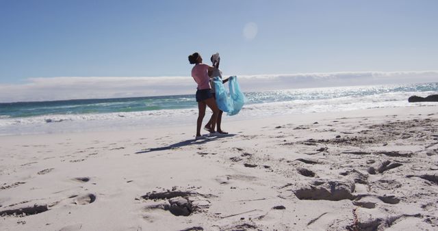 African american couple walking with rubbish sacks and collecting rubbish from the beach. eco beach conservation.