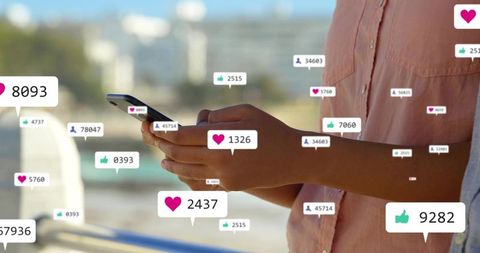 Woman holding smartphone with social media likes and followers icons on coastal boardwalk