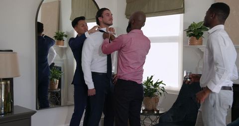 Groom preparing with friends tying bow tie before wedding ceremony
