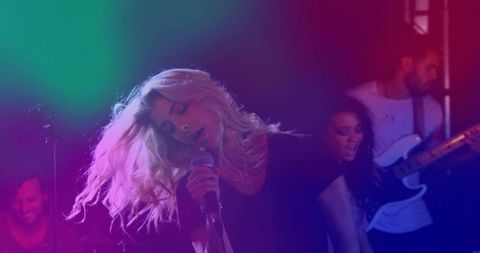 Blonde lead singer performing live club concert with colorful lighting and backing band