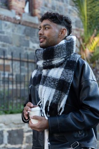 Indian man wearing leather jacket and oversized checked scarf holding coffee cup