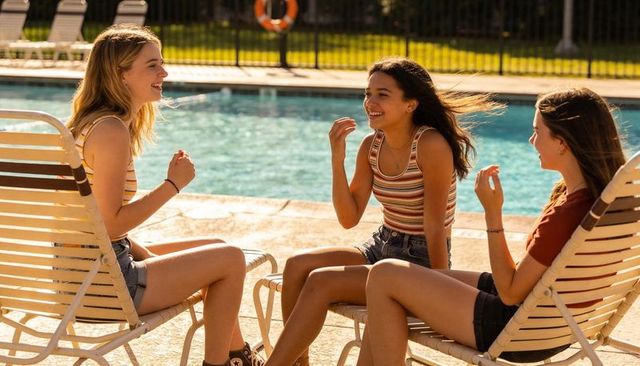 Three teenage friends laughing and chatting poolside in casual summer clothes