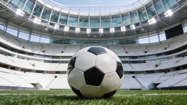 Classic black and white soccer ball resting on lush green pitch inside modern stadium