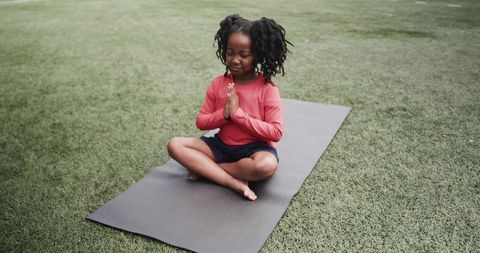 Young african american girl meditating on yoga mat outdoors