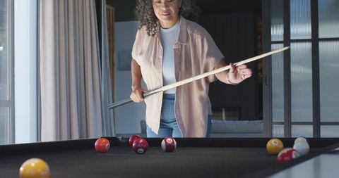 Woman holding cue playing pool at home in casual overshirt and jeans