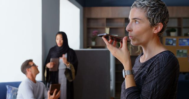 Businesswoman Using Voice Assistant While Colleagues Interact in Background - Download Free Stock Images Pikwizard.com