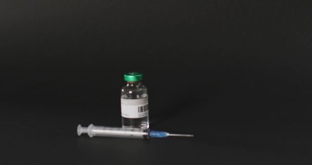 Vial of medicine stands next to a syringe on a black background. Ideal for illustrating medical procedures, vaccination campaigns, pharmaceutical industry, and healthcare information materials.