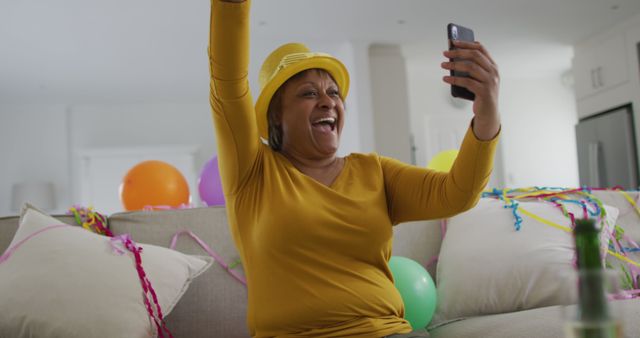 Cheering african american senior woman holding champagne making new year's eve smartphone image call. active, youthful retirement lifestyle, celebrating at home with communication.