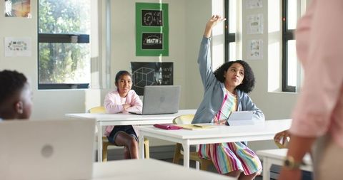African American girl raising hand with tablet in bright classroom during lesson
