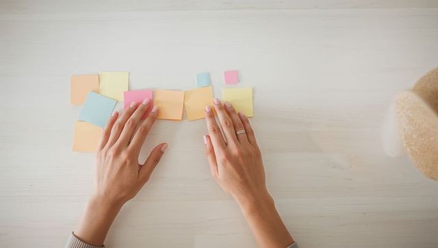 Topdown hands arranging pastel sticky notes on white desk for planning and organization