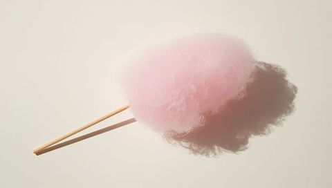 Pale pink cotton candy resting on wooden sticks casting soft shadow on cream surface