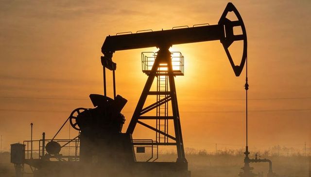 Pumpjack silhouette pumping at golden sunrise on rural oilfield with wellhead focus