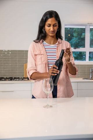 Indian woman opening wine bottle in modern kitchen interior