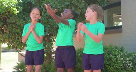 Multicultural schoolgirls clapping and reaching while playing outdoors in green shirts