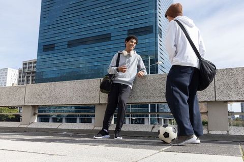 Teenage friends chatting on urban walkway with soccer ball and backpacks