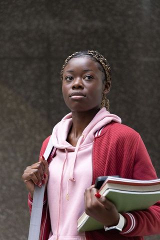 African american teen carrying notebooks and backpack strap on urban campus, confident
