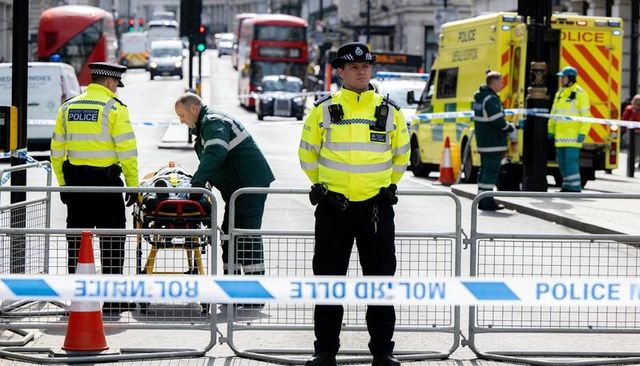 Uniformed police officer guarding cordon with paramedics and ambulances on london street