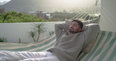 Indian man relaxing on rooftop hammock enjoying warm sunlight and urban terrace calm