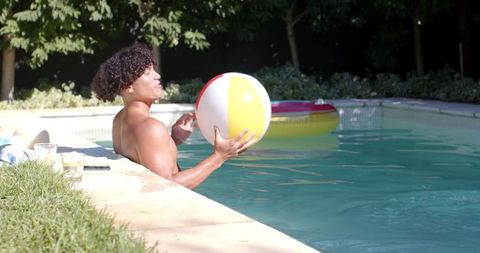 Man Relaxing in Backyard Pool with Beach Ball on Summer Day