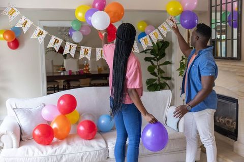 African american couple decorating living room with colorful balloons and birthday banner