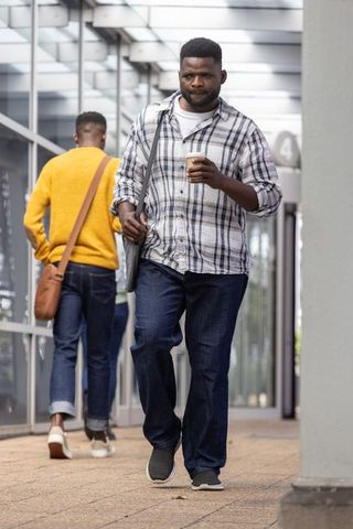 Urban commuters walking through glass corridor carrying coffee and shoulder bags on commute