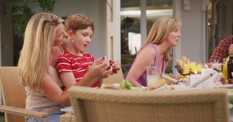 Happy caucasian mother with son on lap at family dinner table in garden - Download Free Stock Photos Pikwizard.com