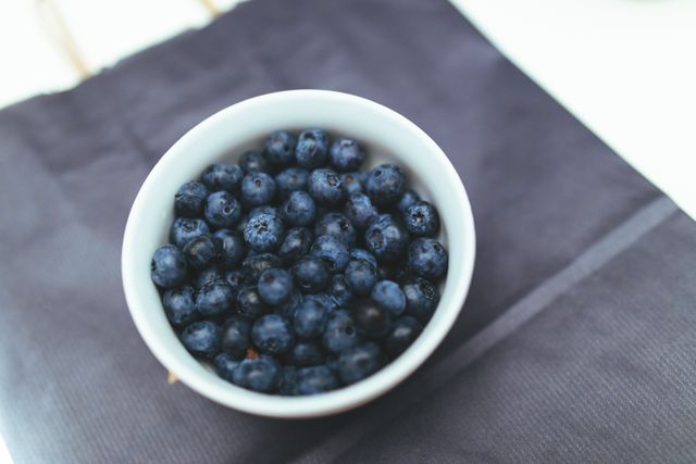 Bowl of fresh blueberries on a dark tablecloth. Ideal for content focusing on healthy eating, diet, fresh produce, recipes, and summer activities. Suitable for blogs, social media, health-related websites, and culinary articles.