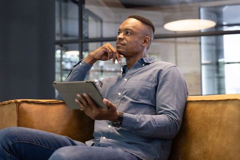 Contemplative African American Professional Using Tablet on Sofa in Office Lounge Casual Business