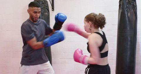 Diverse trainer coaching teen student sparring with pink gloves while coach holding blue mitts