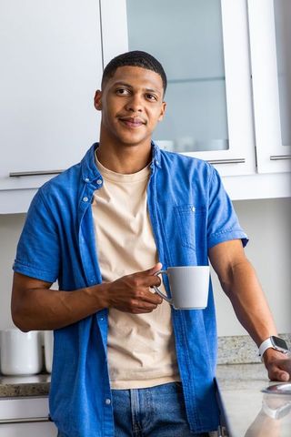 African american man leaning on kitchen counter holding mug wearing smartwatch casual morning