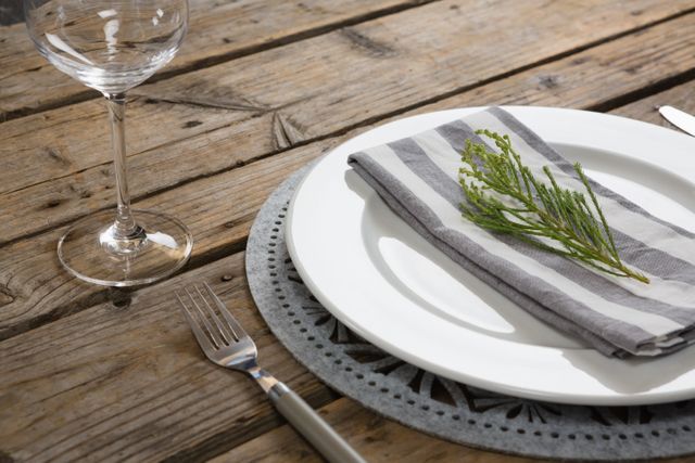 Close-up of fork, butter knife and wine glass with napkin and herb in a plate
