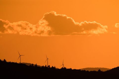 Wind turbines silhouetting against glowing orange sunset sky, dramatic cloud on horizon
