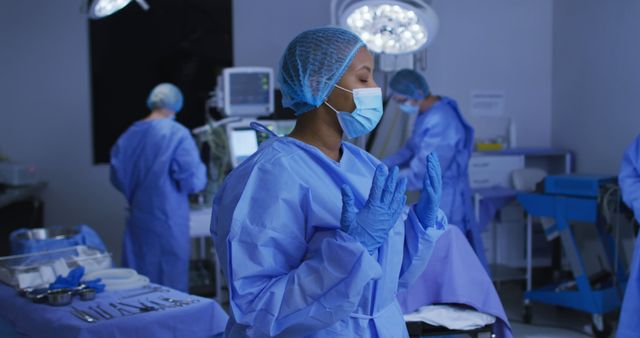 African american female surgeon wearing face mask and protective clothing in operating theatre. medicine, health and healthcare services during covid 19 coronavirus pandemic.