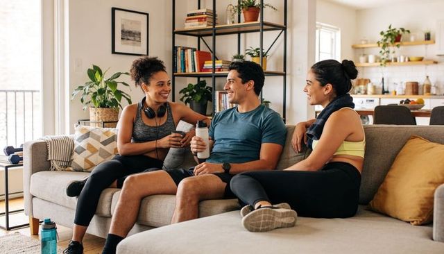 Friends chatting on couch after workout at home - modern fitness lifestyle conversation