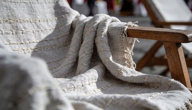 Draping beige woven throw showing stitched grid and frayed tassel over wooden deck chair