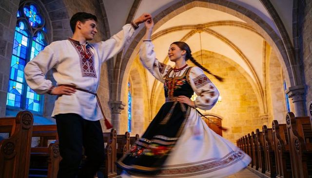 Young couple dancing in embroidered eastern european folk costumes in vaulted stone church