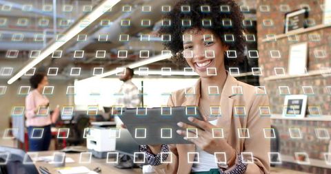 Smiling businesswoman using tablet in modern open office with holographic grid overlay