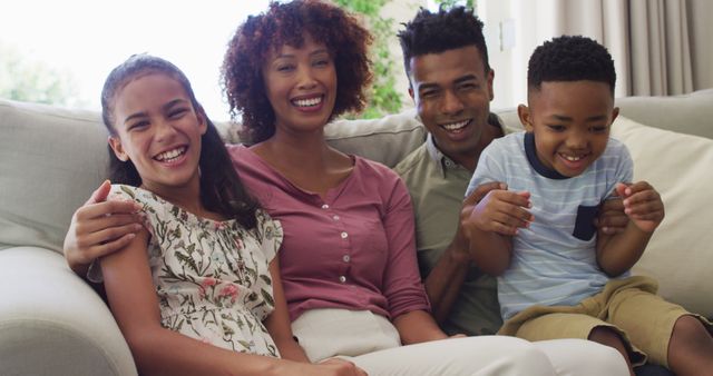 Family sitting together on couch in living room, everyone smiling and appearing joyful. Use for themes around home life, family bonding, children's happiness, and parental relationships.