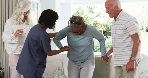 Professional Caregiver Assists Elderly Woman At Home With Friends Nearby