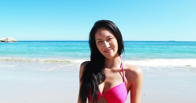 Asian woman in pink bikini smiling on sunny beach. Great for travel promotions, summer vacation ads, lifestyle blogs, and tropical getaway marketing.