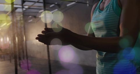 Female athlete rubbing chalked hands preparing for workout in dim gym silhouette with bokeh