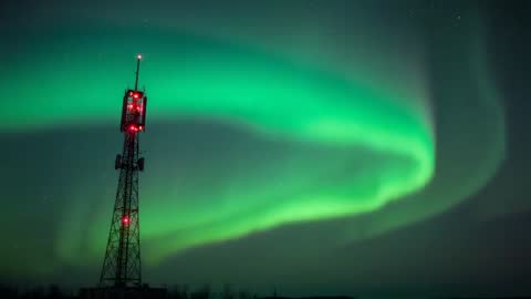 Aurora Borealis swirling over communications tower with red warning lights, starry sky