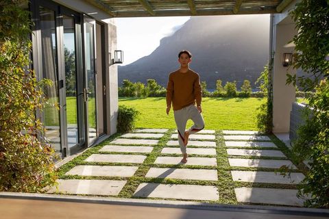 Asian man balancing on one leg on stepping stones at modern patio with mountain view