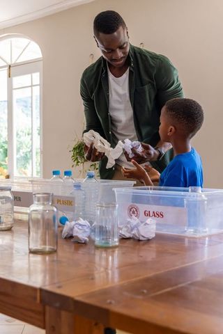 African american father teaching son recycling by sorting plastic and glass together at home